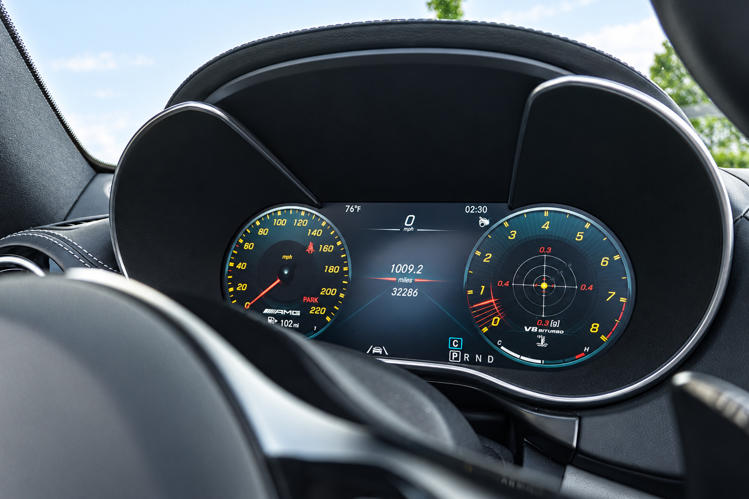 Digital instrument cluster of the AMG GT C Roadster seen through the steering wheel, black cabin around it