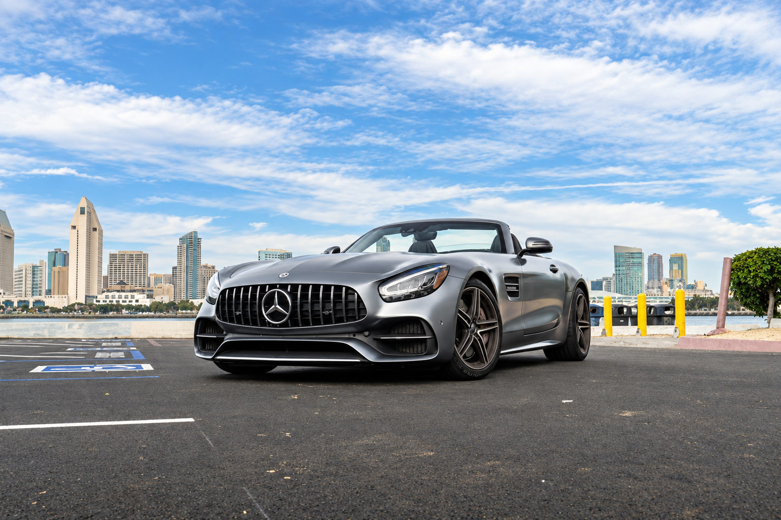 Front three-quarter of the satin silver AMG GT C Roadster with the roof down and downtown San Diego across the bay