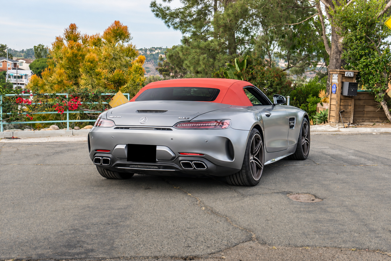 Rear three-quarter of the satin silver AMG GT C Roadster with the red fabric top up, quad exhaust tips visible