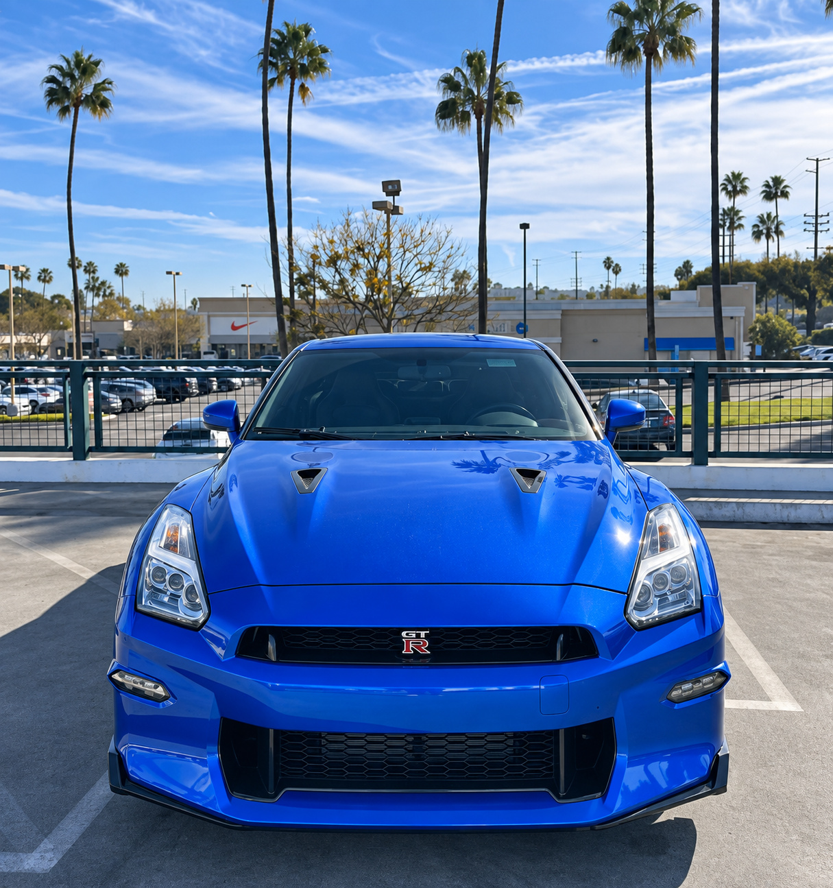 Head-on view of the Bayside Blue Nissan GT-R showing the honeycomb mesh grille, hood vents and palm trees behind