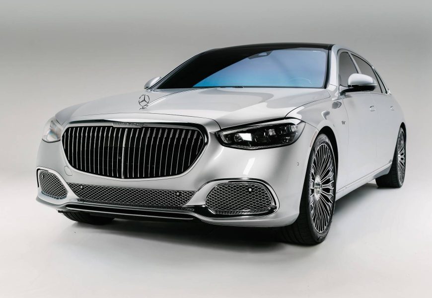Front corner of the pearl white Maybach S680 with the vertical chrome grille and headlights lit