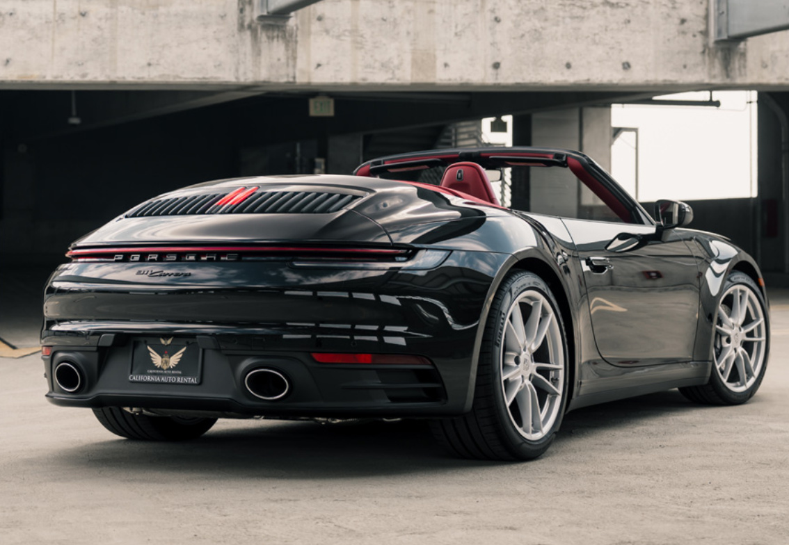 Rear three-quarter of the black Porsche 911 Carrera Cabriolet, top down, red cabin showing over silver wheels