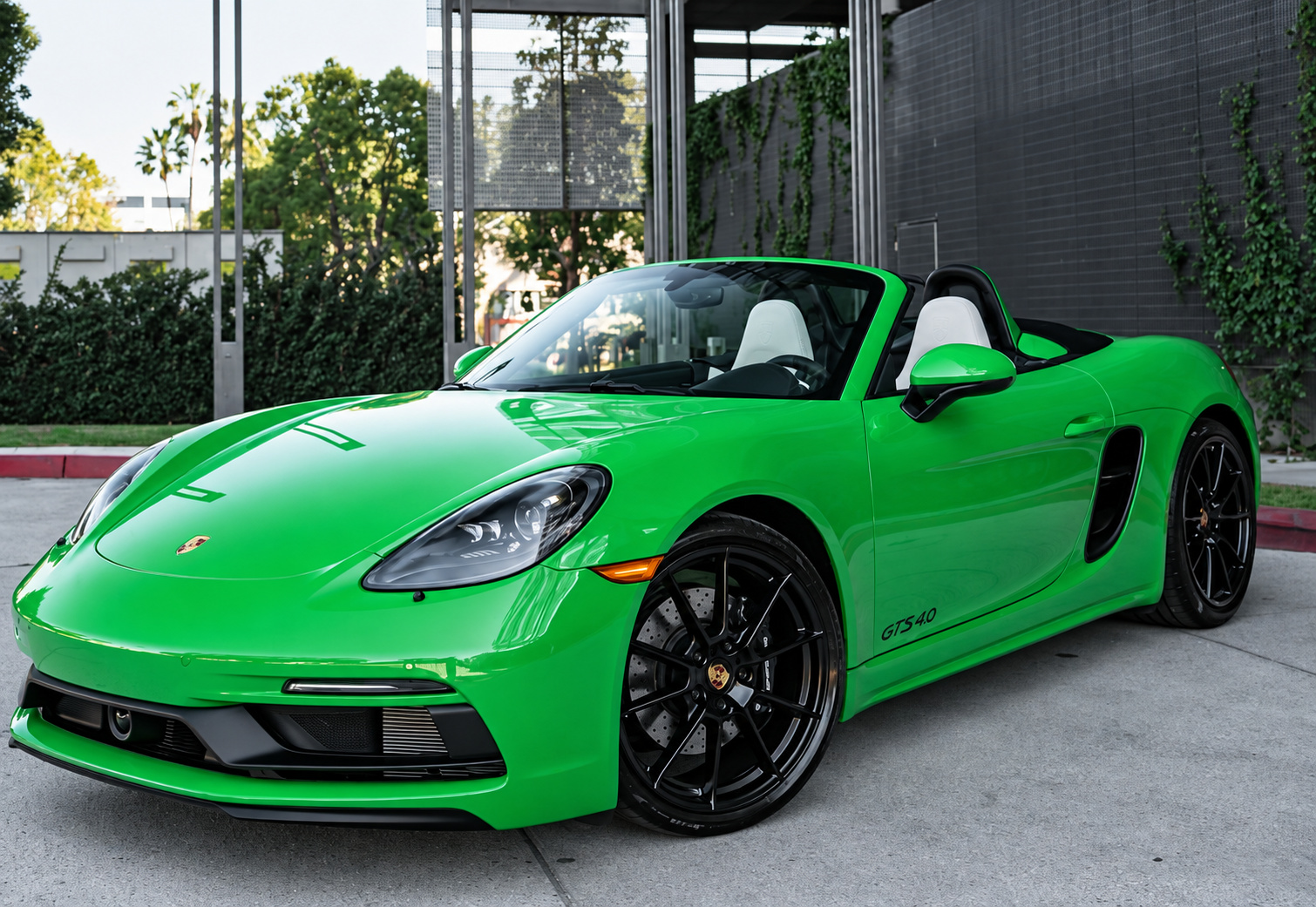 Python Green Porsche 718 Boxster GTS 4.0 with the top down, front three-quarter view beside an ivy-covered wall