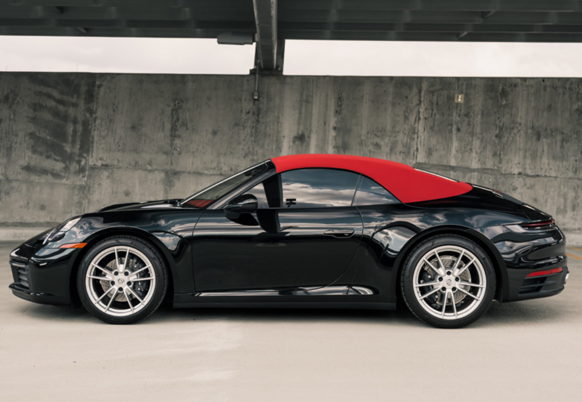 Side profile of the black Porsche 911 Carrera Cabriolet with the red roof up and silver wheels