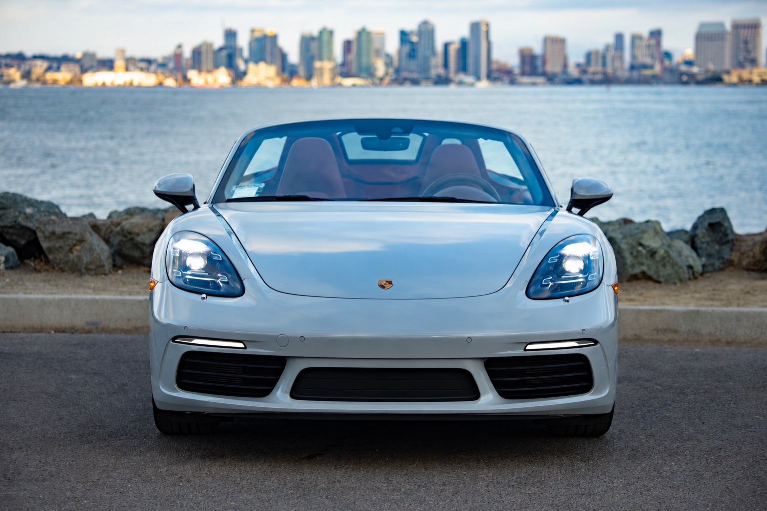 Head-on view of the chalk white 718 Boxster T, roof down, red seats showing through the windshield