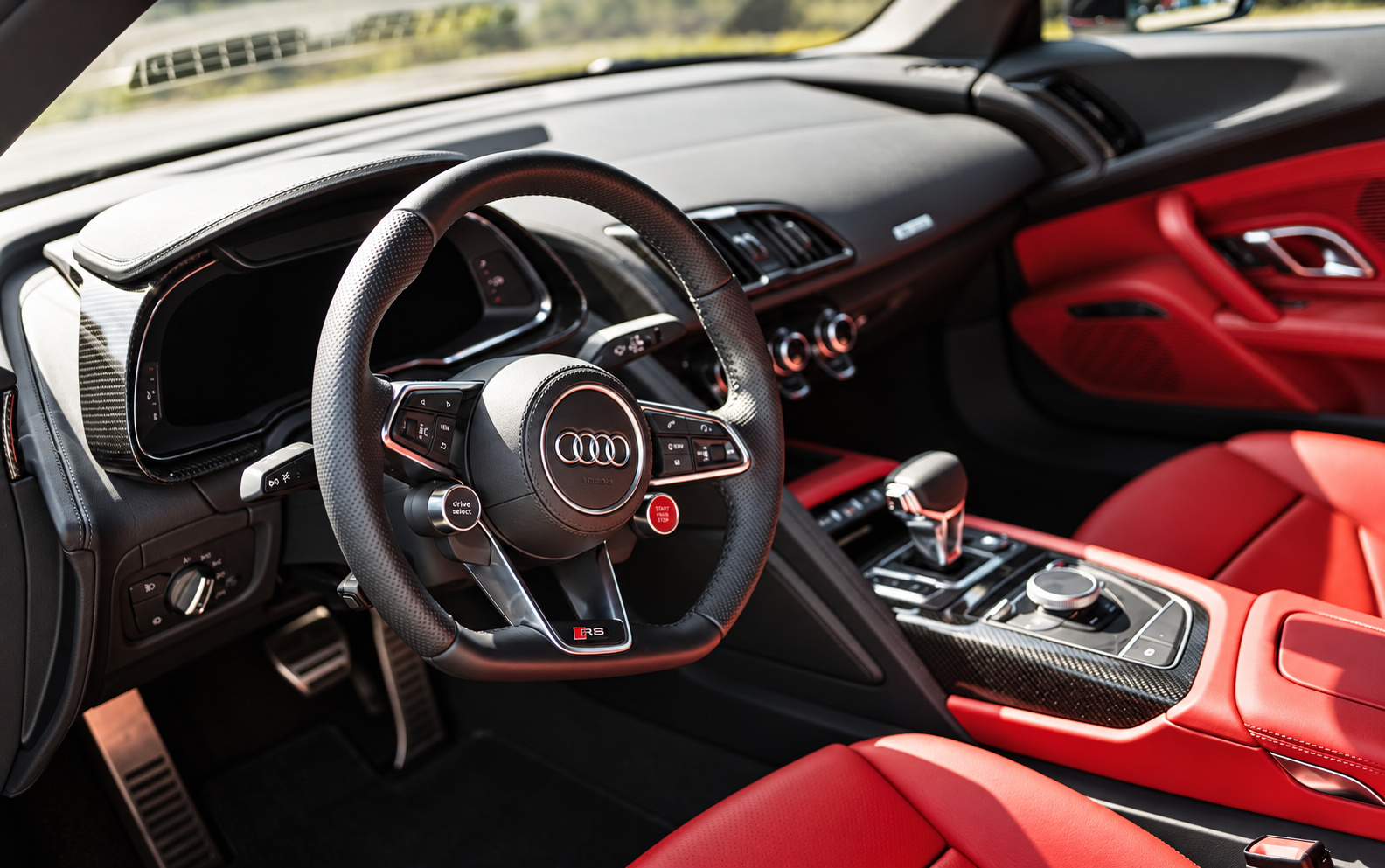 Driver's side of the Audi R8 V10 Coupe cabin, red leather, flat-bottom wheel, red start button and carbon fiber trim