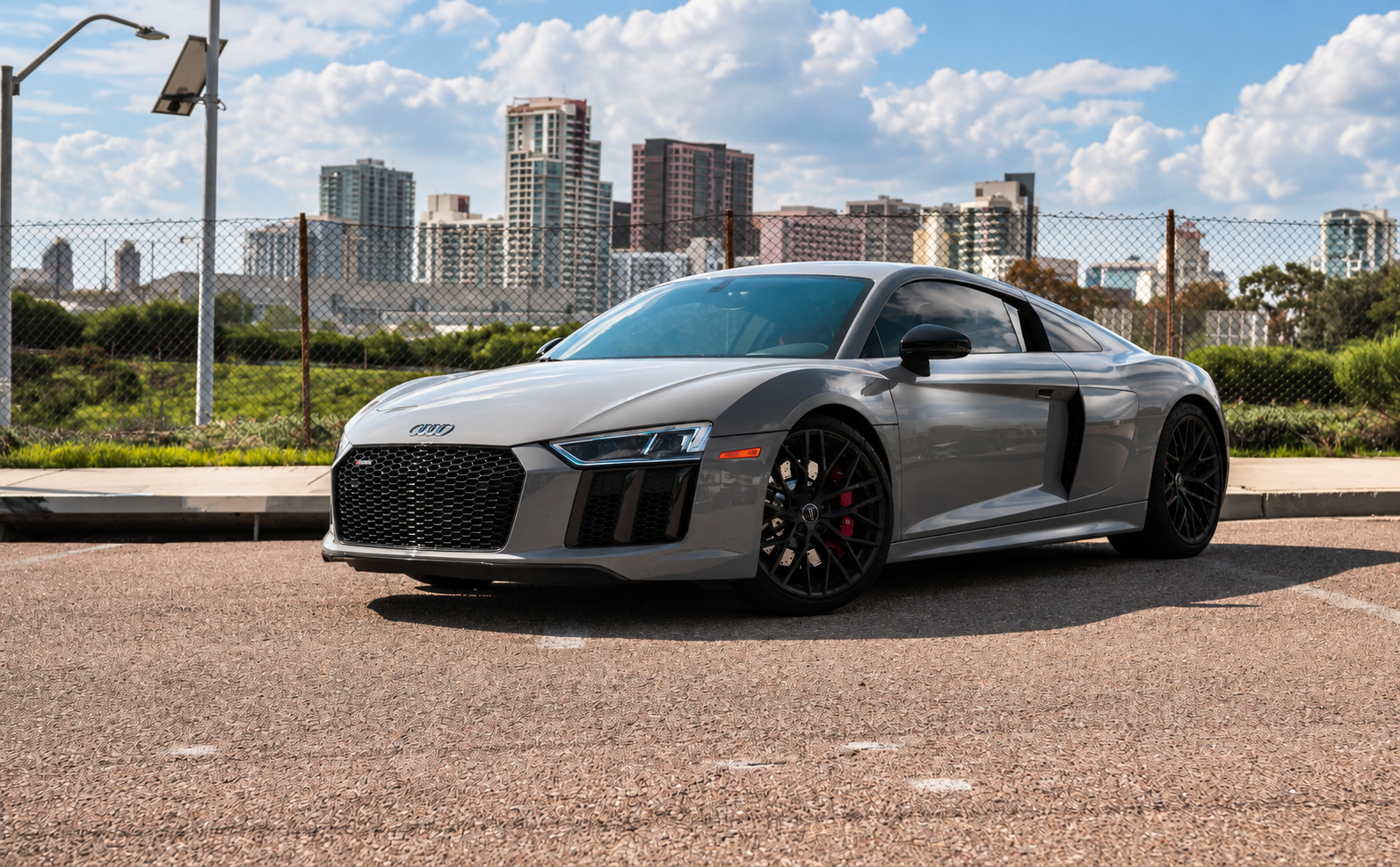 Nardo grey Audi R8 V10 Coupe parked in a lot with the downtown San Diego skyline behind it, black wheels and red calipers