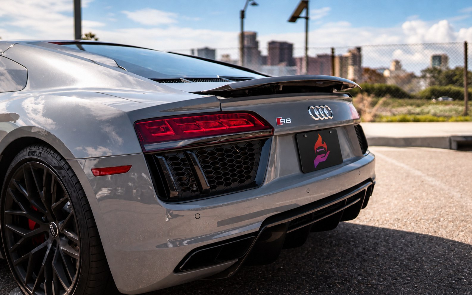 Rear three-quarter of the Nardo grey Audi R8 V10 Coupe with the spoiler up and the San Diego skyline in the distance