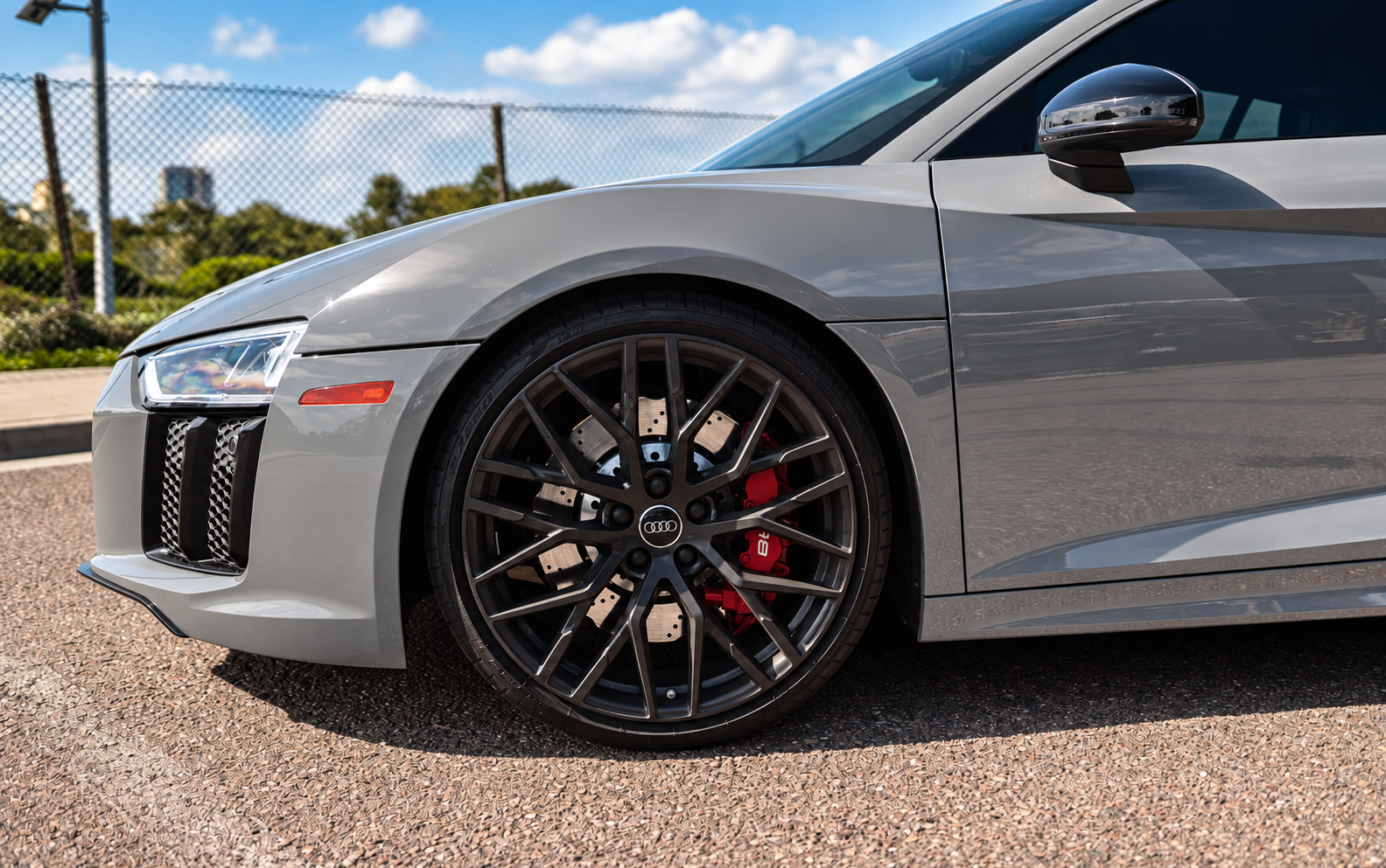 Front wheel of the Nardo grey Audi R8 V10 Coupe, black spokes and red caliper beside the honeycomb side intake