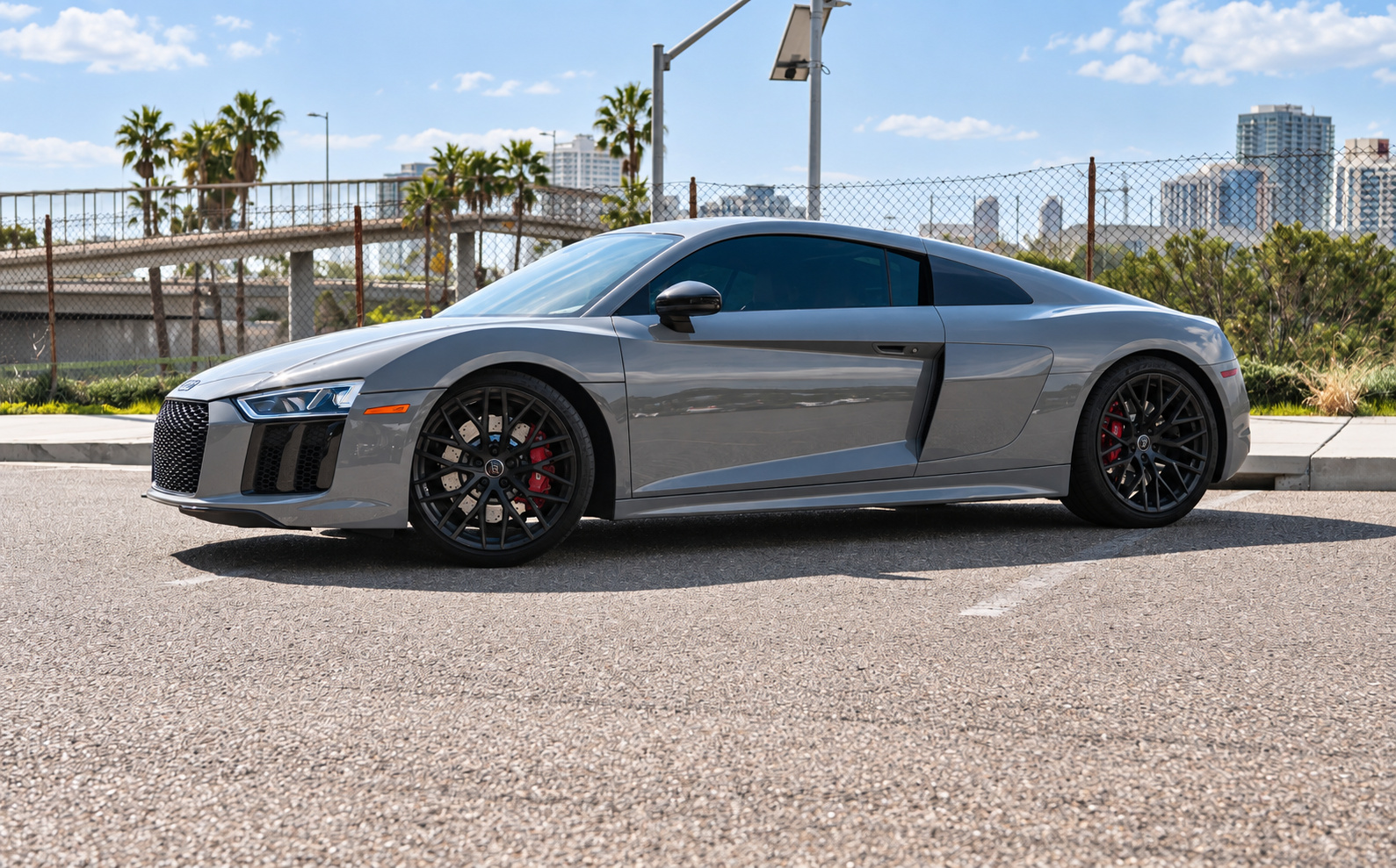 Front three-quarter of the Nardo grey Audi R8 V10 Coupe in a San Diego lot, black side blade and black wheels in the sun