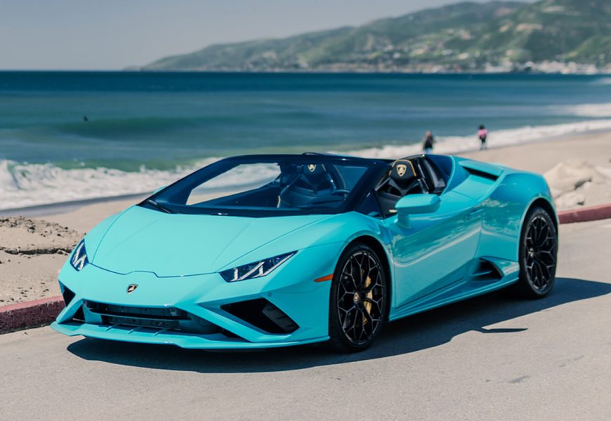 Turquoise Lamborghini Huracan Evo Spyder with the roof down, front three-quarter view on the sand lot at Zuma Beach in Malibu
