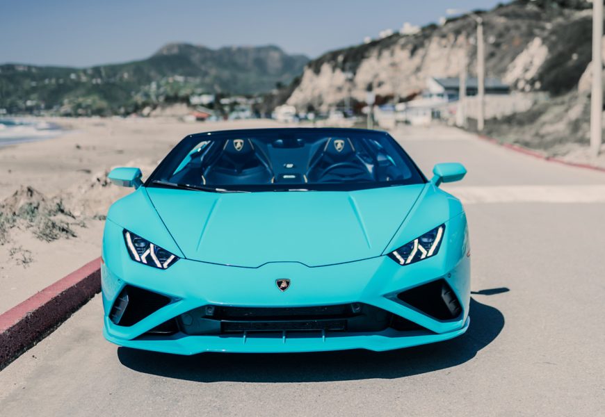 Head-on view of the turquoise Lamborghini Huracan Evo Spyder parked at the beach lot in Malibu with the bluffs behind