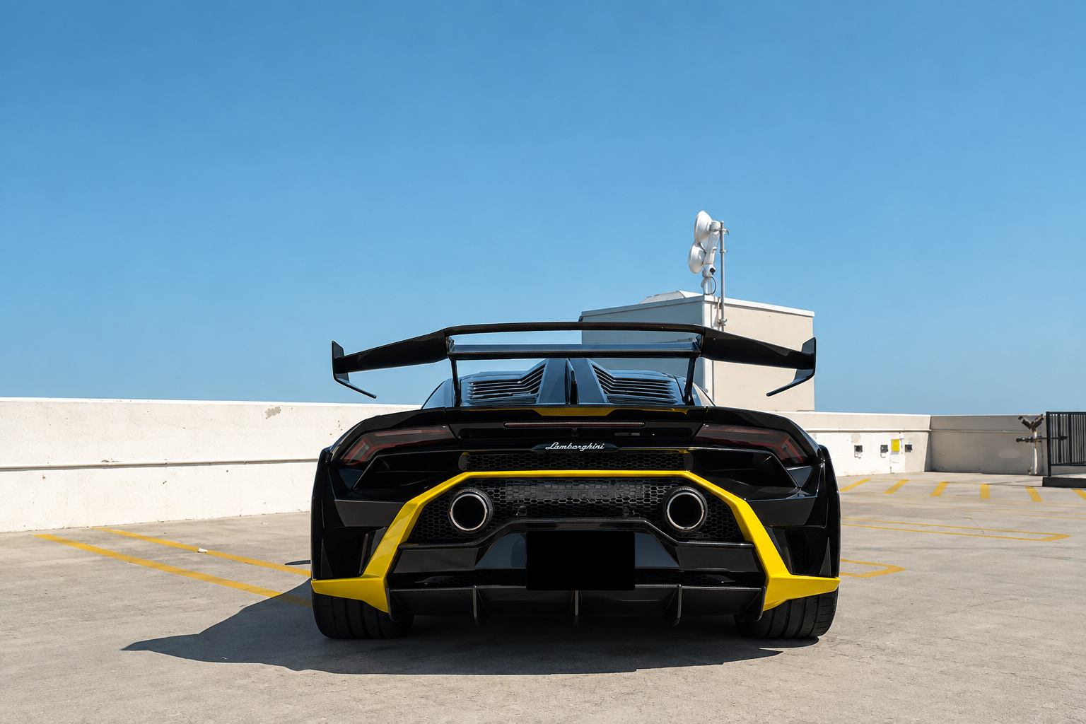 Rear view of the black Huracan STO, shark fin, carbon rear wing and yellow diffuser lip on a rooftop deck