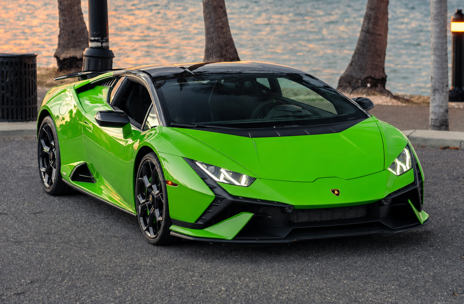Front three-quarter of the green Huracan Tecnica beside palm trees at sunset with water behind