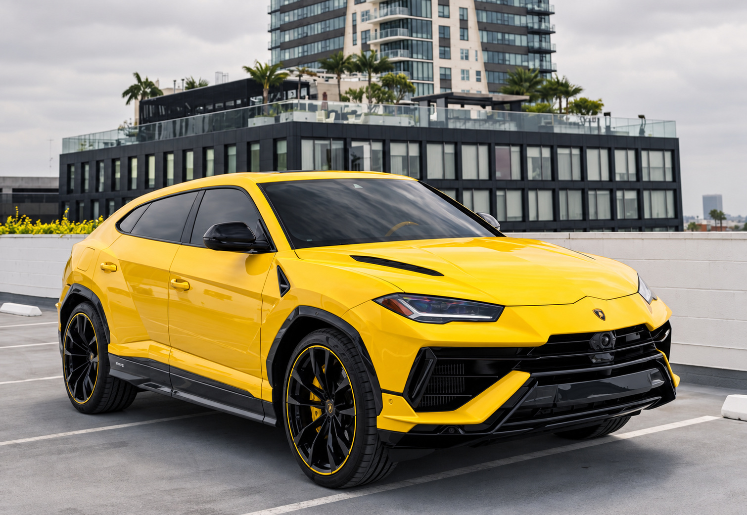 Yellow Lamborghini Urus on a rooftop parking deck with a glass tower behind, front three-quarter view