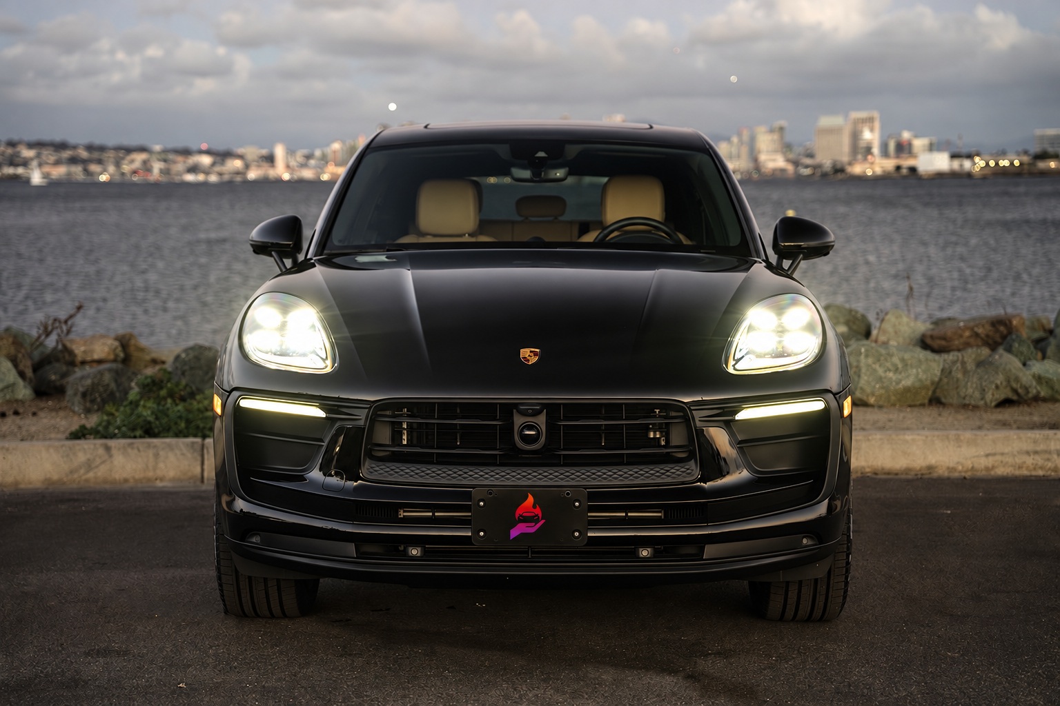 Head-on view of the black Porsche Macan with the LED headlights on, cream seats showing through the windshield