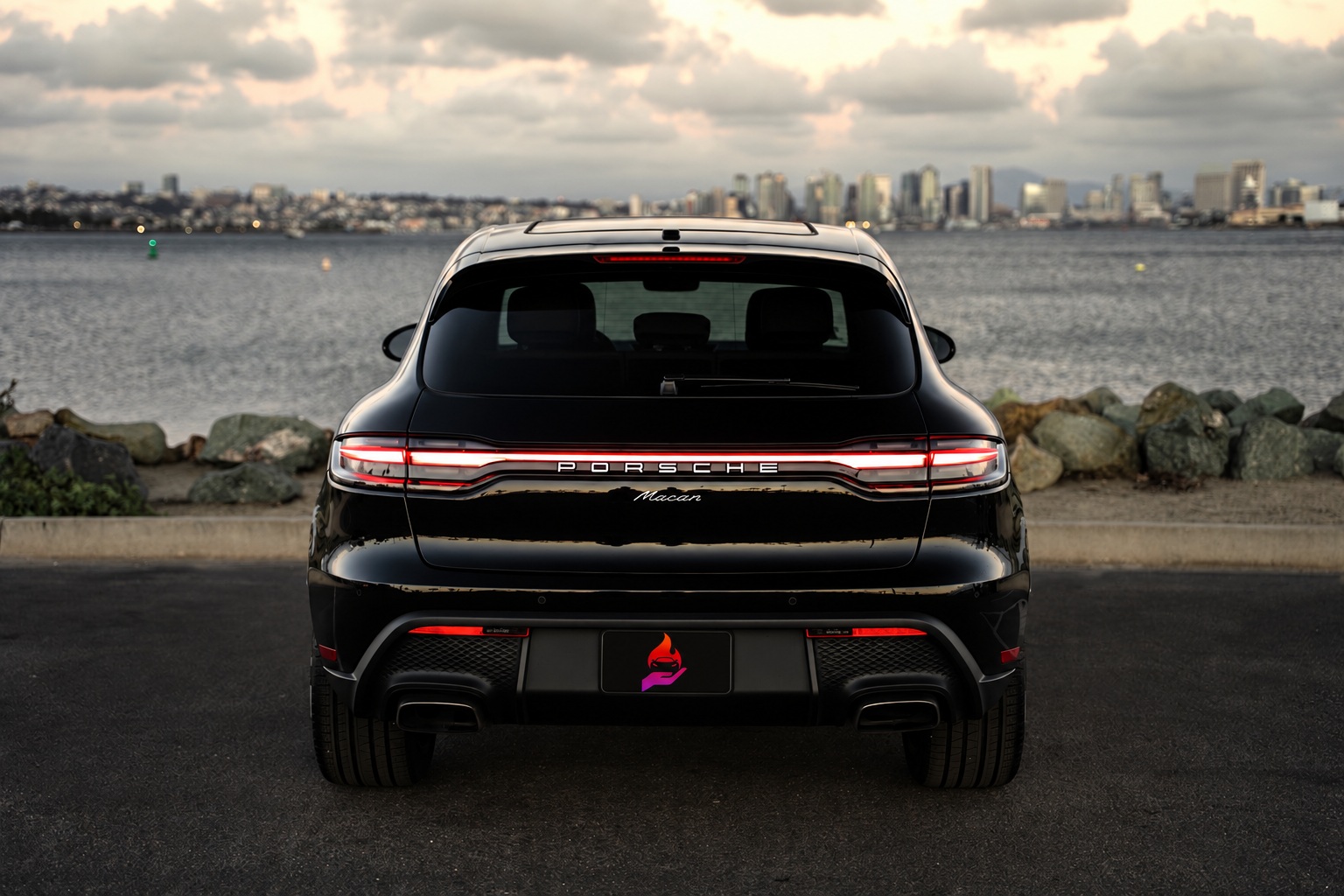 Straight rear view of the black Macan with the Porsche script across the light bar, San Diego bay behind