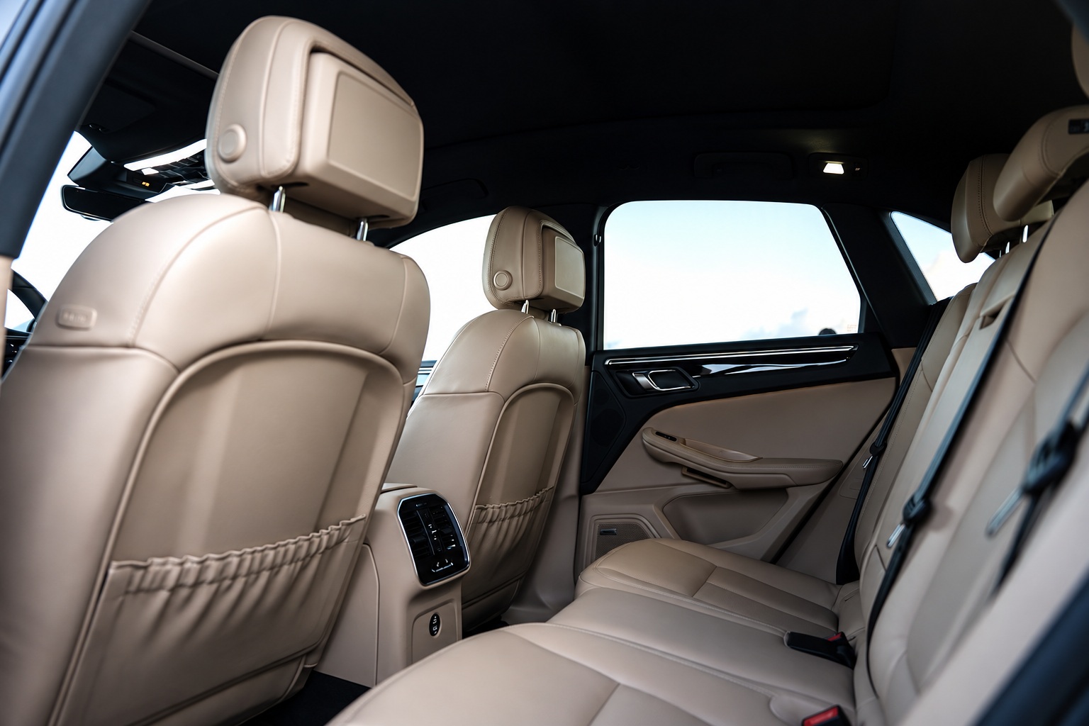 Cream leather rear bench of the black Porsche Macan with the rear door open, headrests and the centre armrest