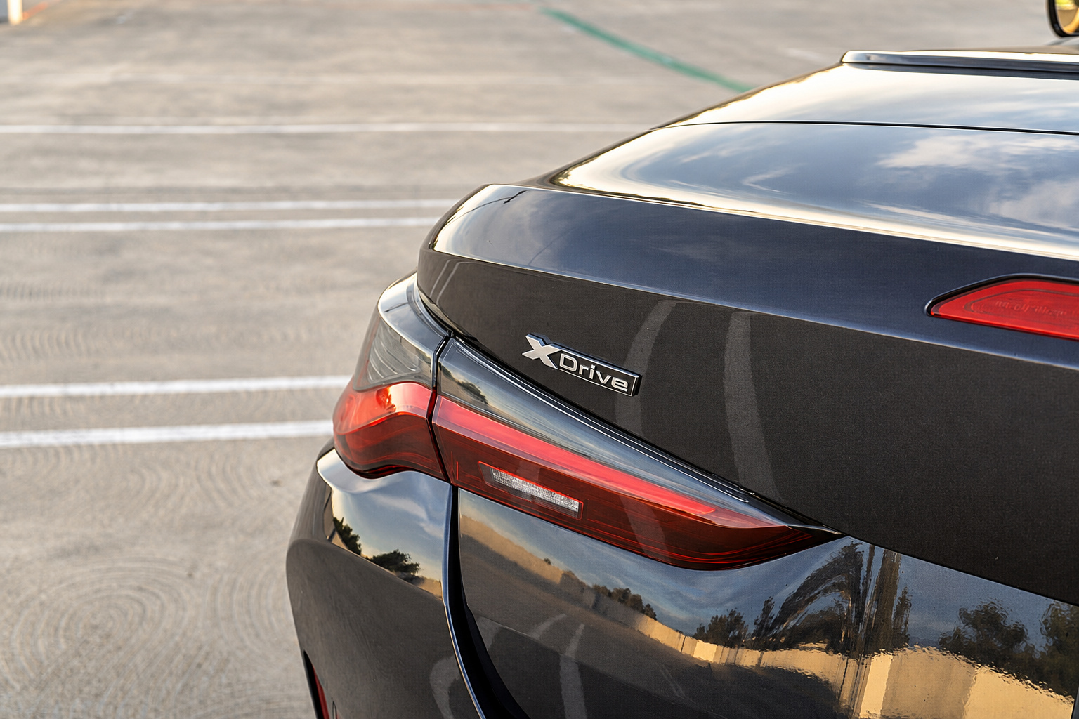 Tail light and xDrive badge on the black BMW M4 Competition Convertible, the trunk lid reflecting the evening sky