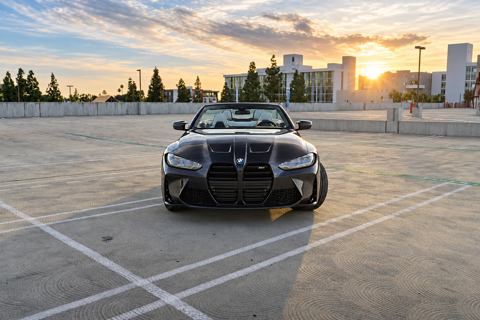 Head-on view of the black M4 Competition Convertible with the sun setting behind it, kidney grille and roof down