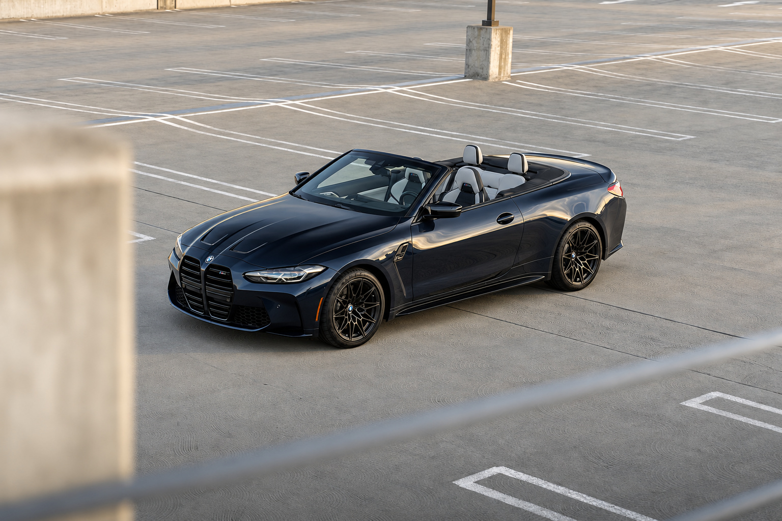 Black BMW M4 Competition Convertible seen past a concrete pillar, roof down, ivory white seats catching the light