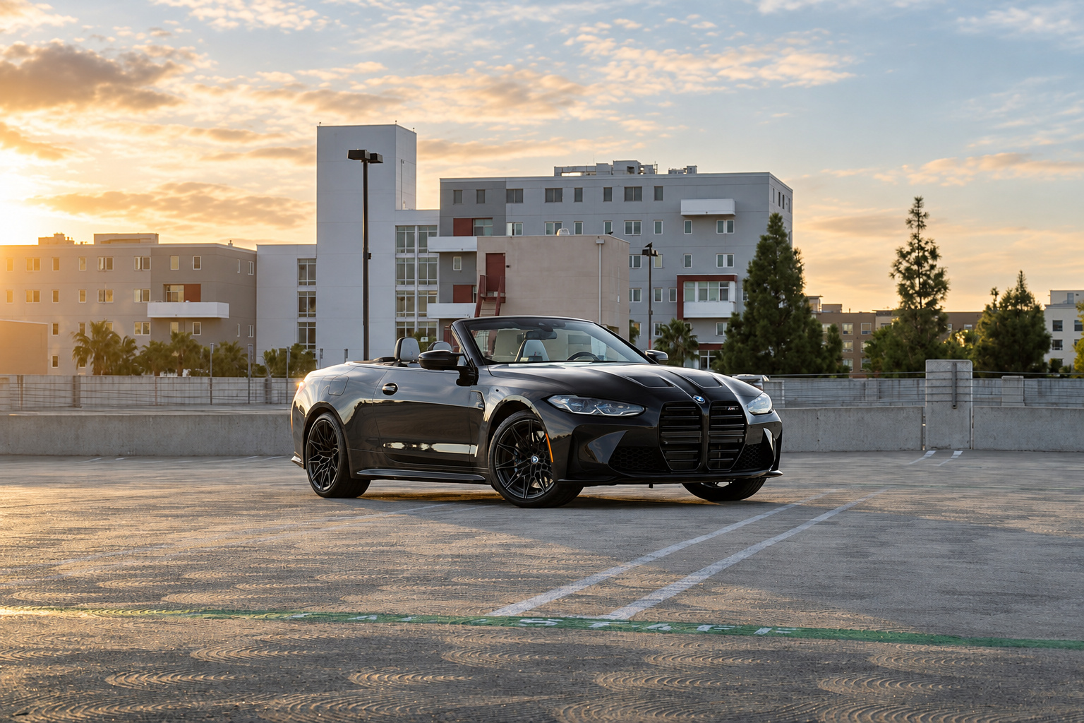 Black BMW M4 Competition Convertible with the roof down on a parking structure roof at sunset, ivory seats visible