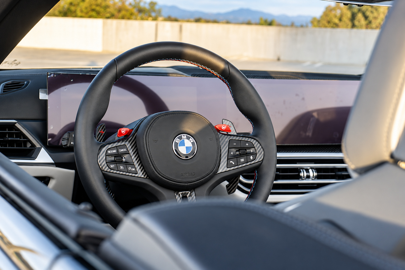 Steering wheel of the M4 Competition Convertible with the red M1 and M2 buttons and the curved display behind it
