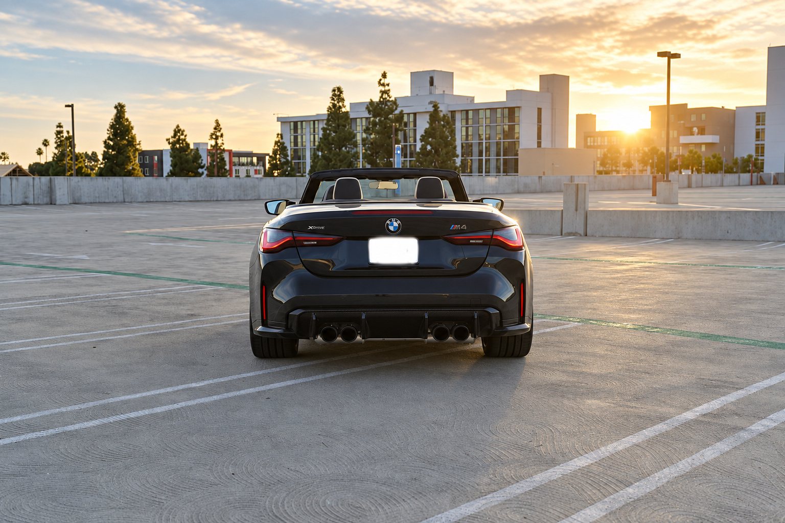Rear view of the black BMW M4 Competition Convertible with the roof down, quad exhaust and the sun low on the horizon