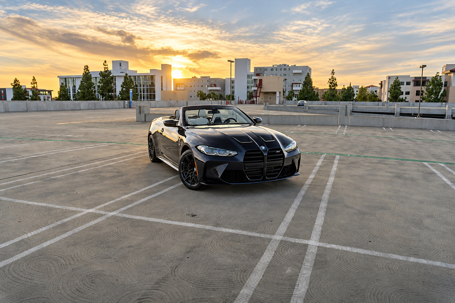 Front three-quarter of the black M4 Competition Convertible at sunset, roof down, parked across the lines on an open rooftop