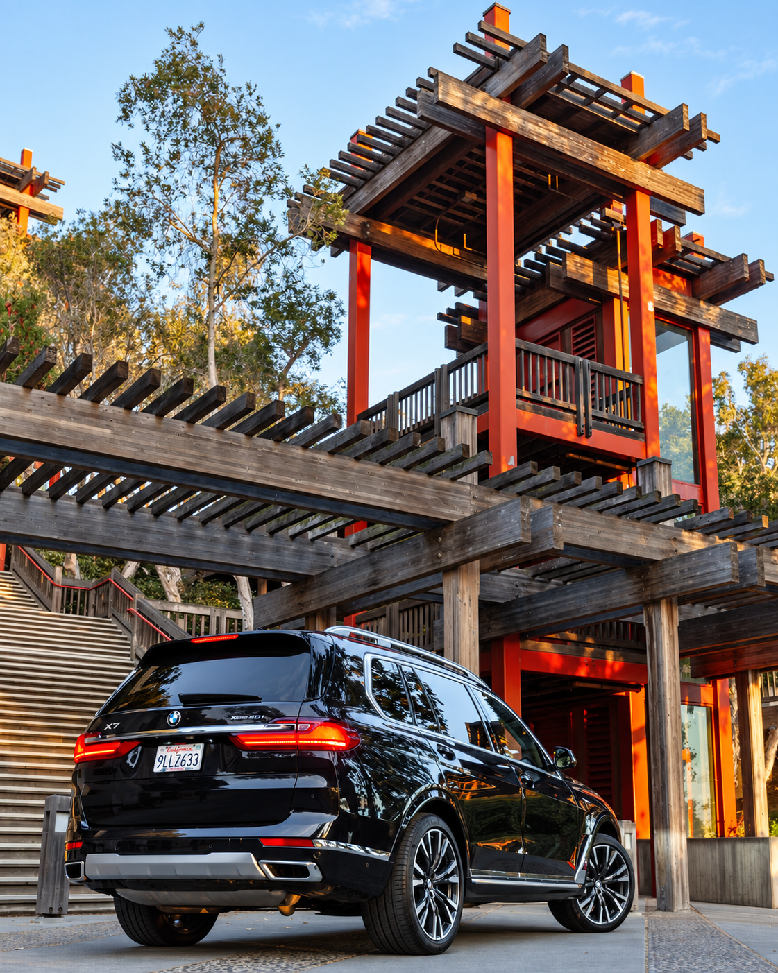 Black BMW X7 parked below a red wooden pagoda tower, chrome trim catching the evening light