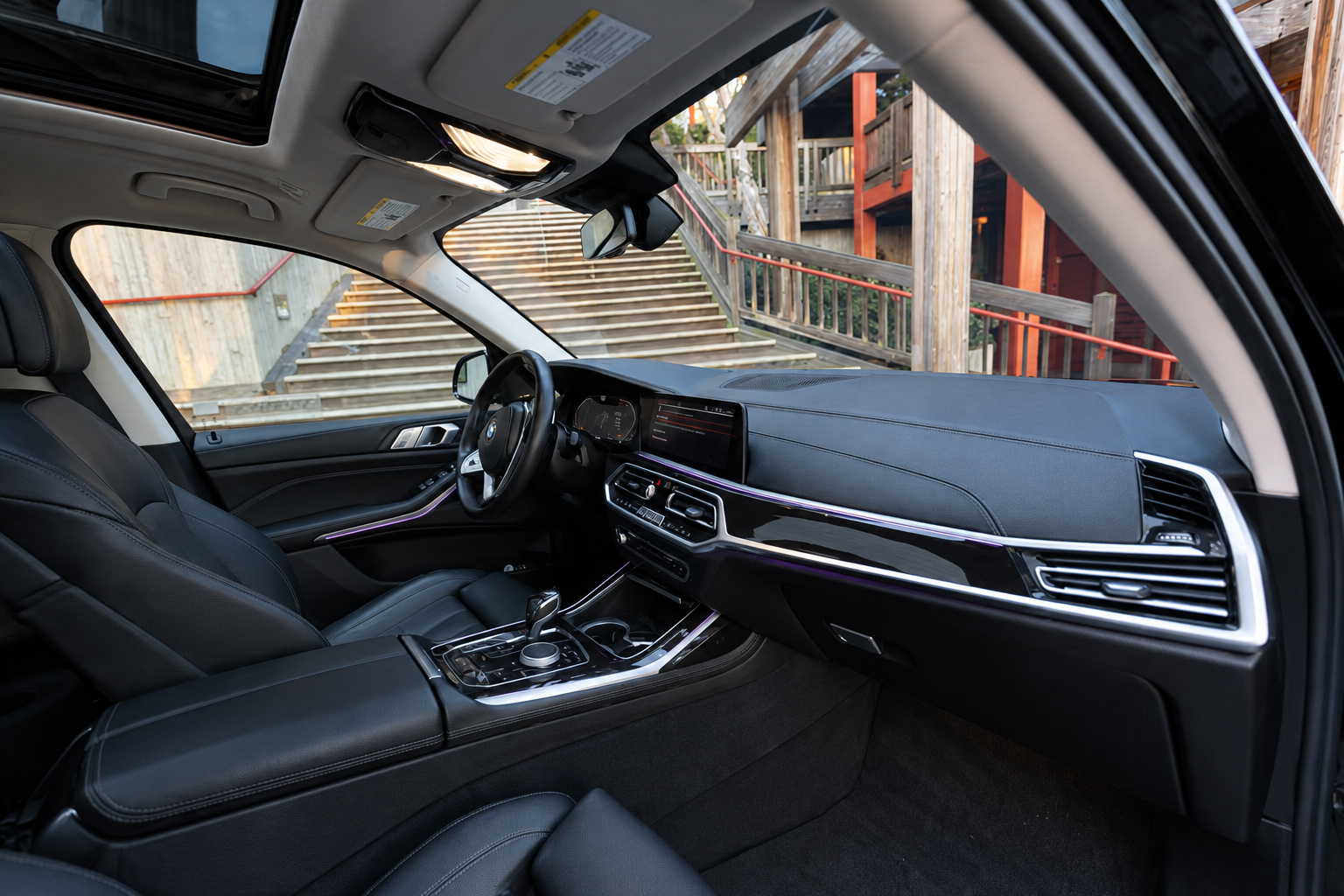 Interior of the black BMW X7 from the passenger side showing the black leather seats and the panoramic glass roof