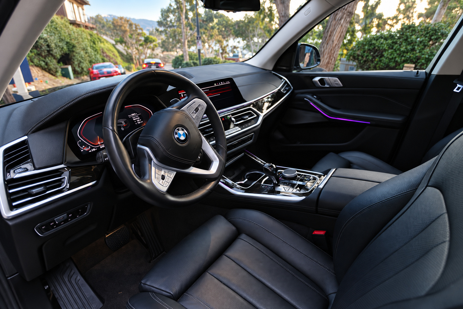 Driver's view of the BMW X7 dash, black leather, steering wheel, twin screens and brushed metal across the console