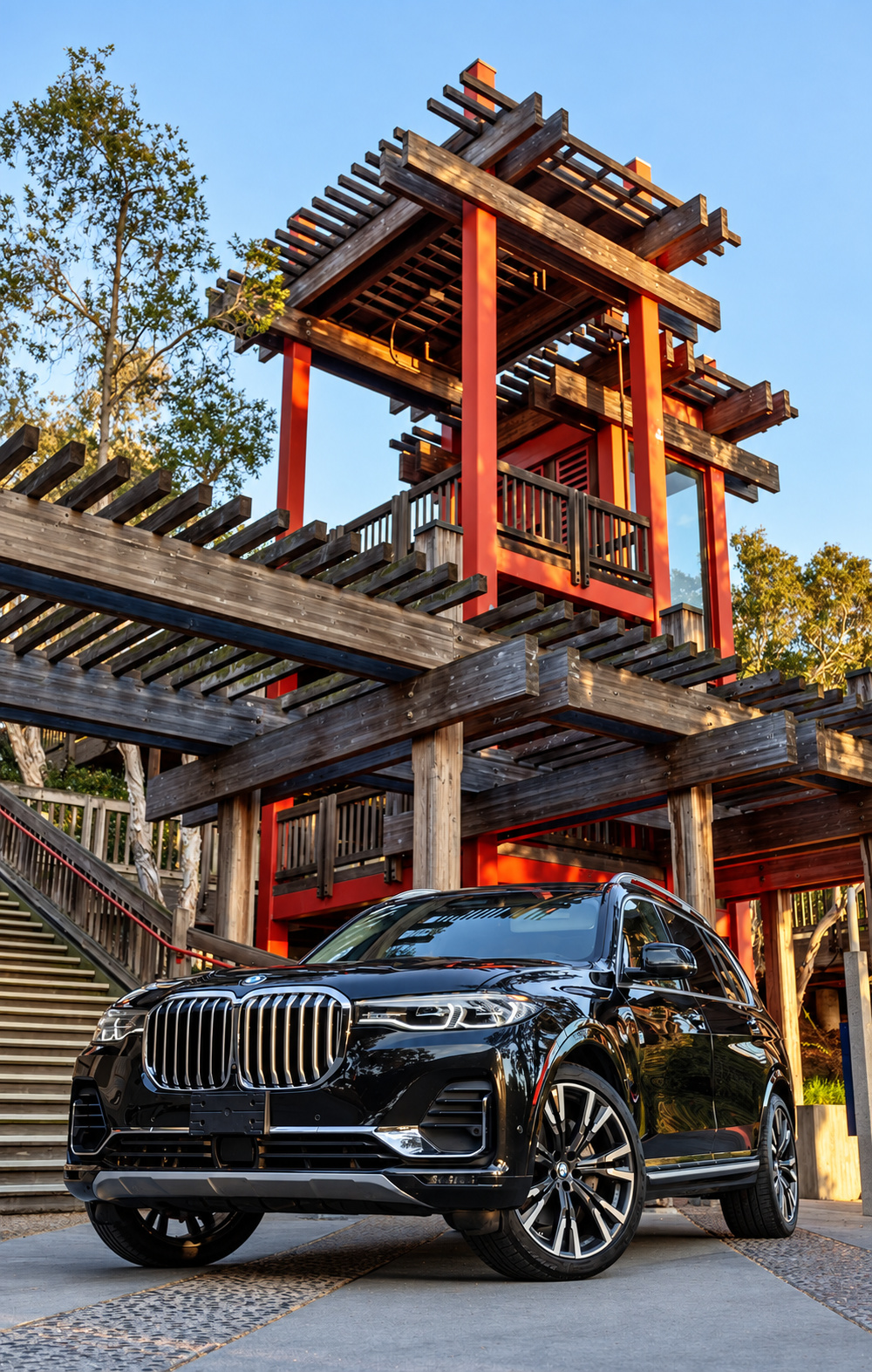 Front three-quarter of the black BMW X7 with the chrome kidney grille, beneath red pagoda stairs