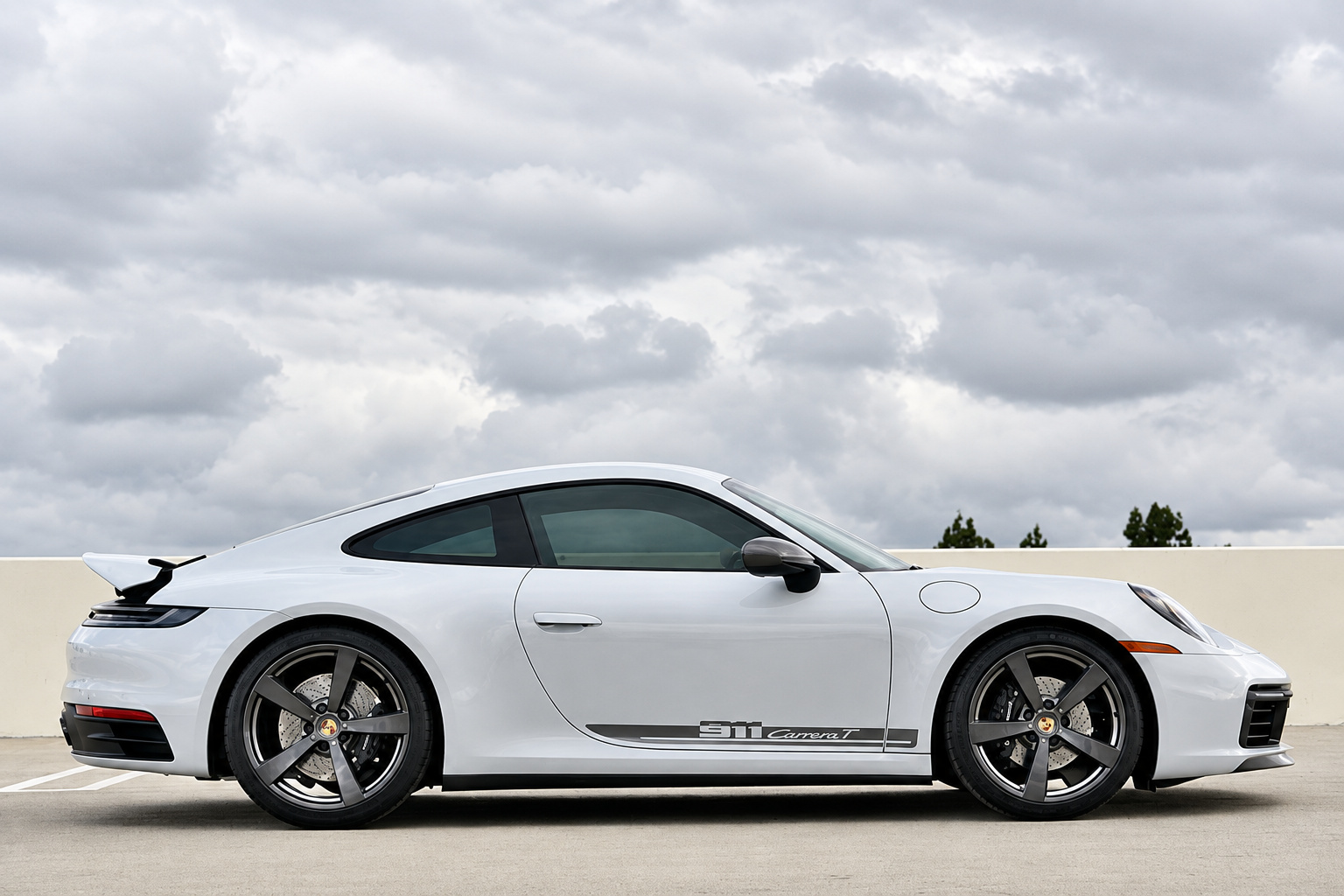 Side profile of the Chalk Porsche 911 Carrera T with the rear spoiler raised and dark grey wheels