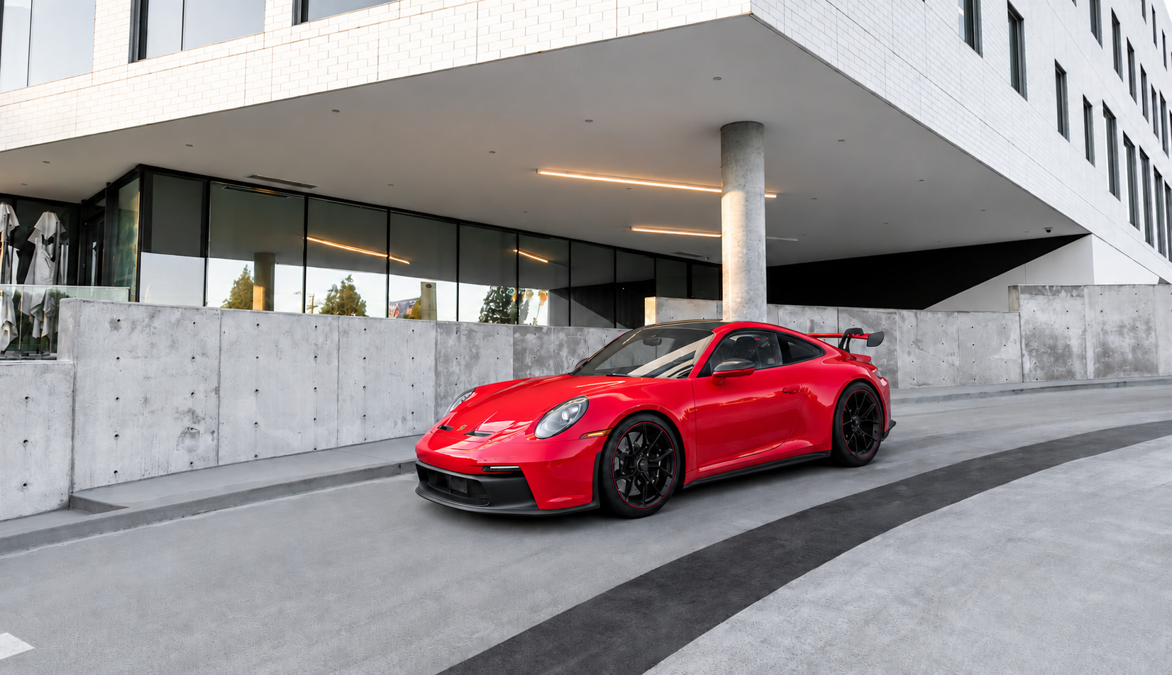 Guards Red Porsche 911 GT3 with the rear wing, front three-quarter view outside a modern concrete and glass building