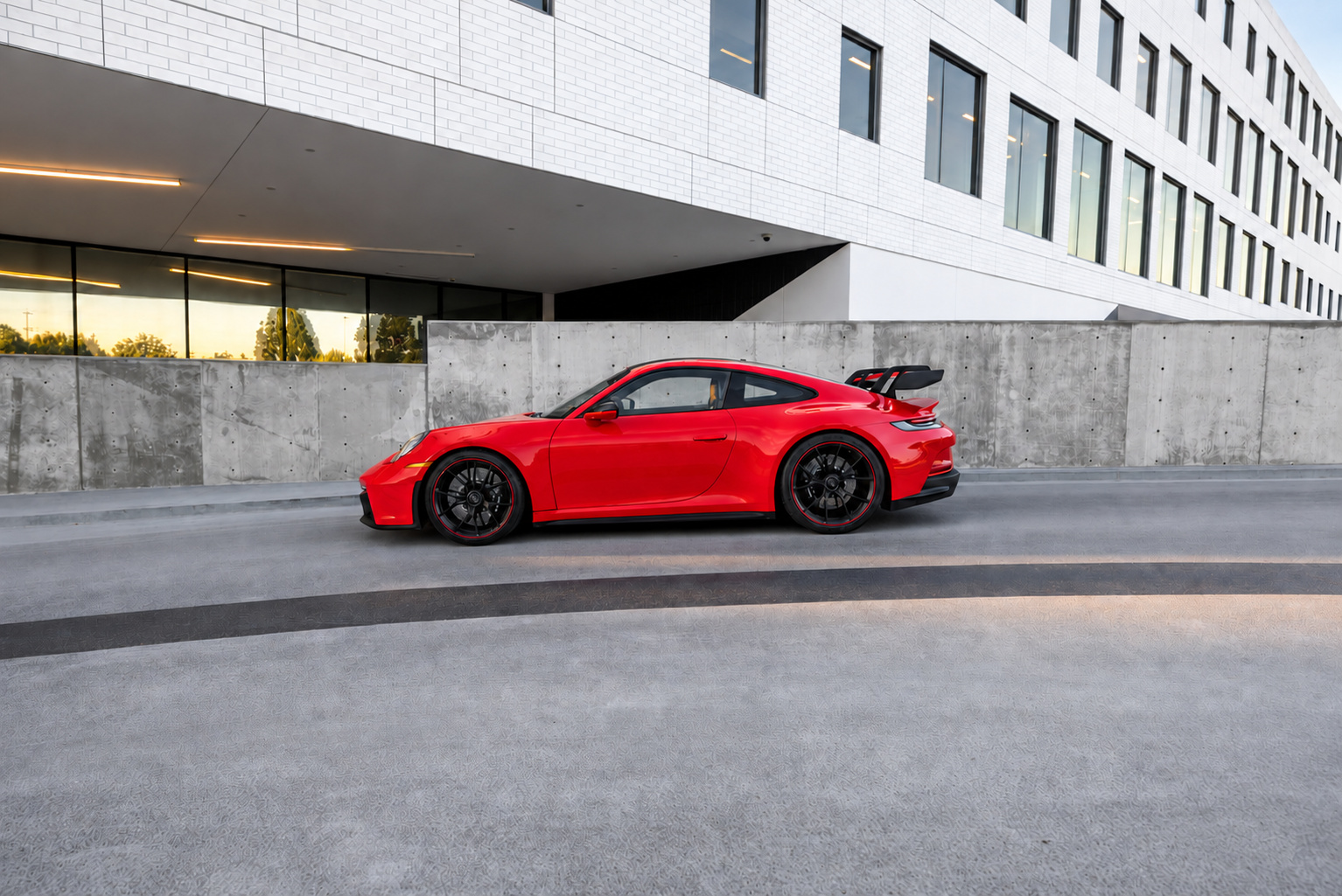 Side profile of the Guards Red Porsche 911 GT3 on black wheels beside a concrete wall