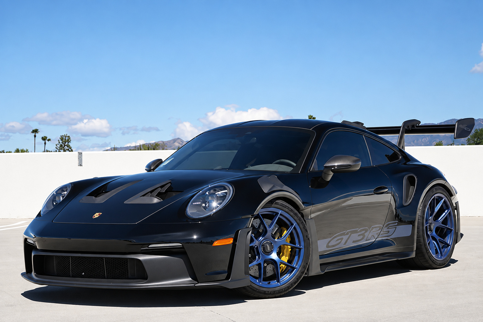 Black Porsche 911 GT3 RS Weissach on blue magnesium wheels with yellow calipers, front three-quarter on a rooftop deck