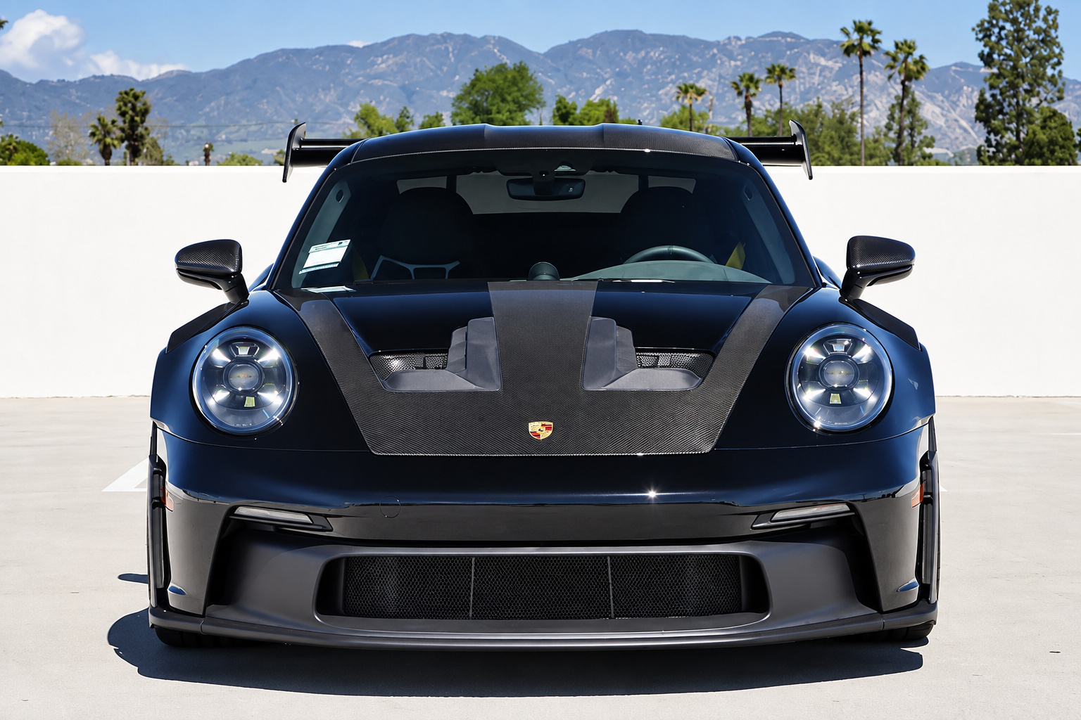 Black Porsche 911 GT3 RS Weissach head on with the wing above the roof and mountains in the distance
