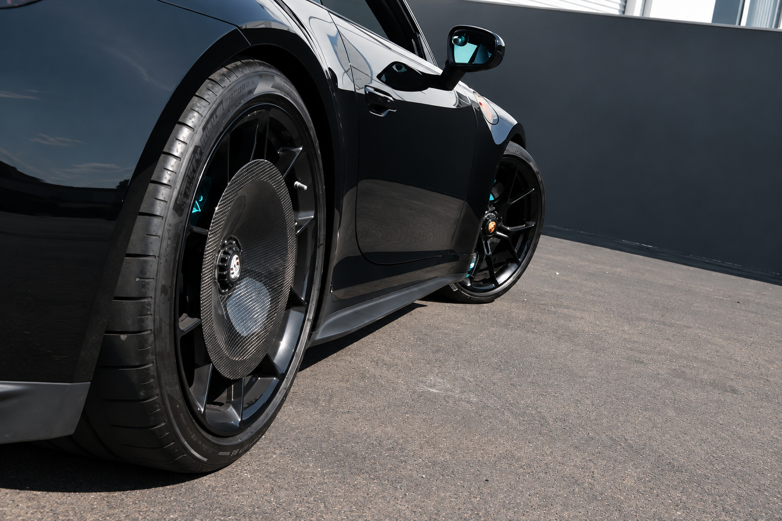 Rear centre-lock wheel of the Porsche 911 GT3 Touring with the Miami Blue brake caliper behind black spokes