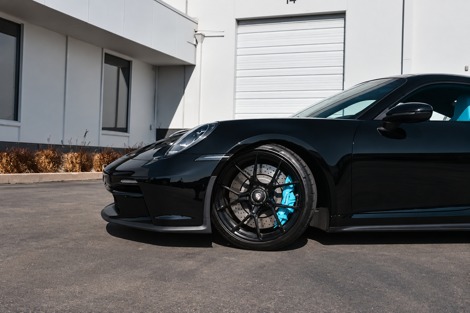 Front corner of the black Porsche 911 GT3 Touring showing the splitter, headlight and blue caliper