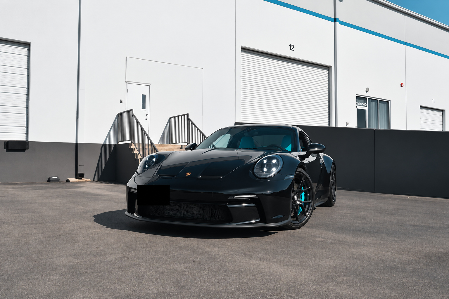 Black Porsche 911 GT3 Touring head on outside a white warehouse, blue calipers visible through the wheels