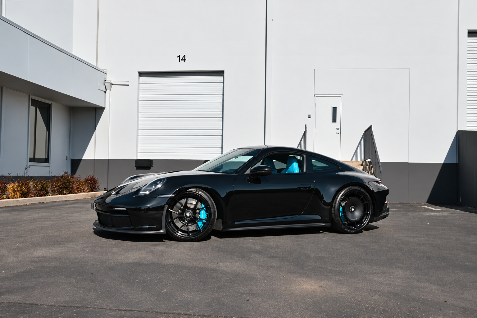 Black Porsche 911 GT3 Touring with blue calipers, front three-quarter view in a warehouse lot