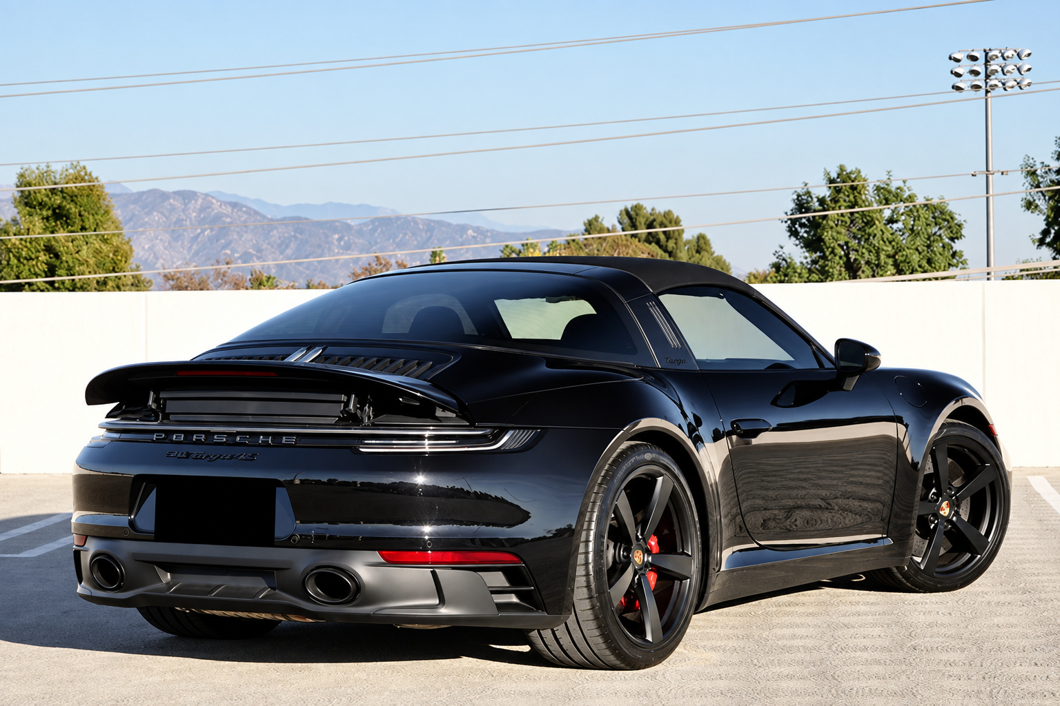 Rear three-quarter of the black Porsche 911 Targa 4 GTS with the spoiler raised and mountains behind
