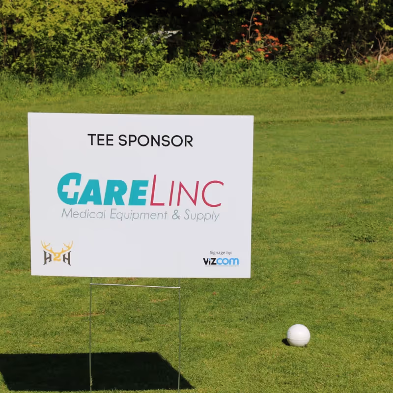 Golf tee sign for CareLinc Medical Equipment & Supply on green next to a golf ball.