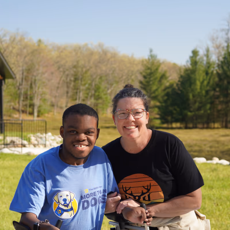 Smiling man in blue shirt and woman in black shirt pose outdoors with a grassy background.