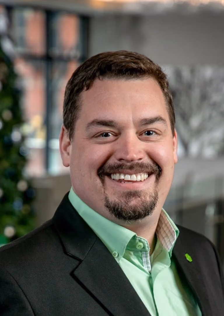 Smiling man with goatee wearing a black suit jacket and light green shirt indoors.
