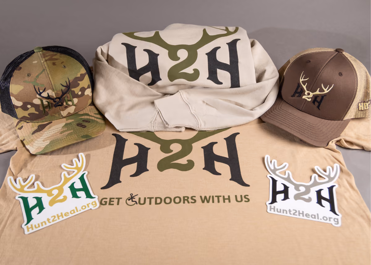 Camo and brown caps, hooded sweatshirt, and T-shirt with H2H logo and Hunt2Heal.org stickers.