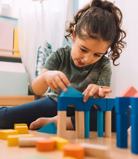 Young girl with curly hair playing with colorful wooden blocks indoors.