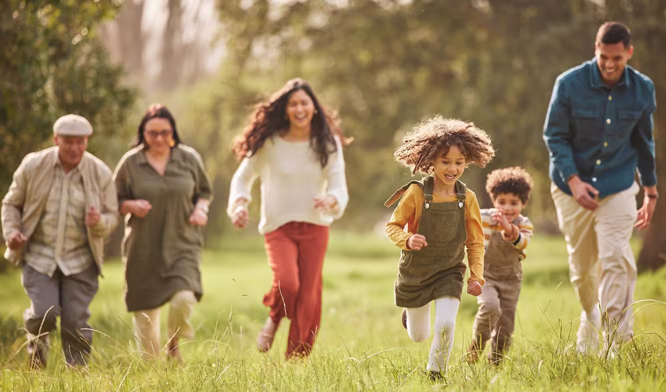 Multi-generational family with two children running and playing on grass in a park.