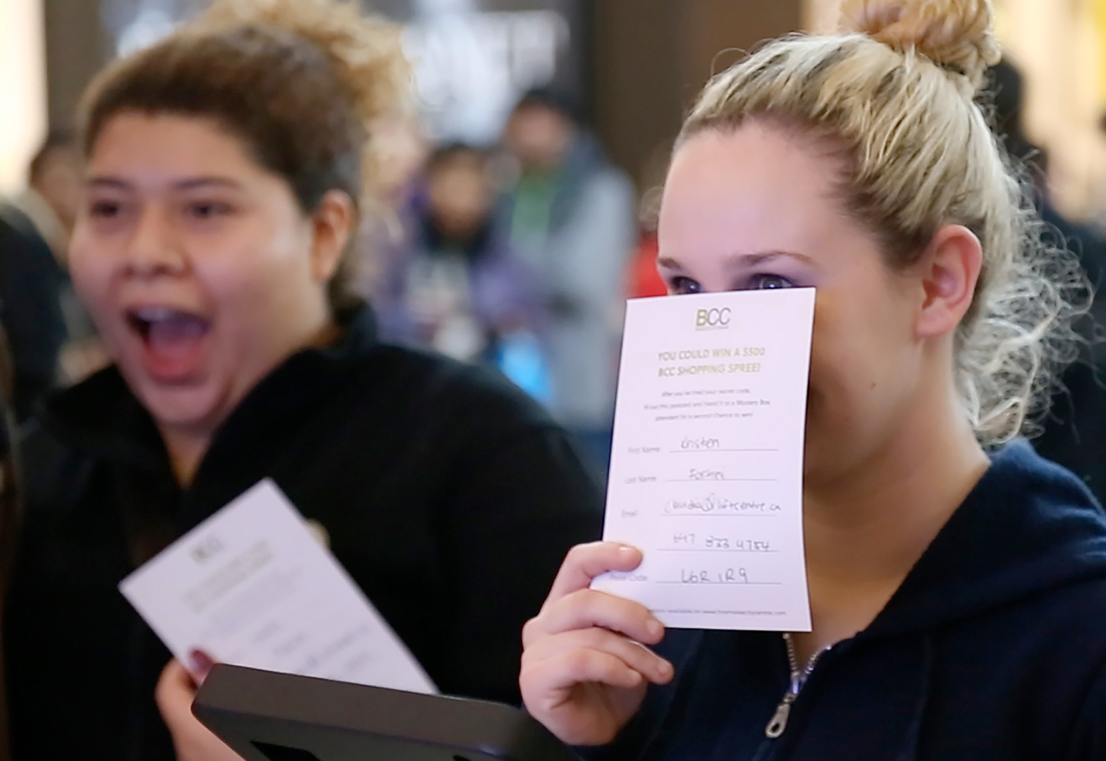 Close up photograph of a young women hiding her smile behind a postcard and looking with anticipation at something we can't see